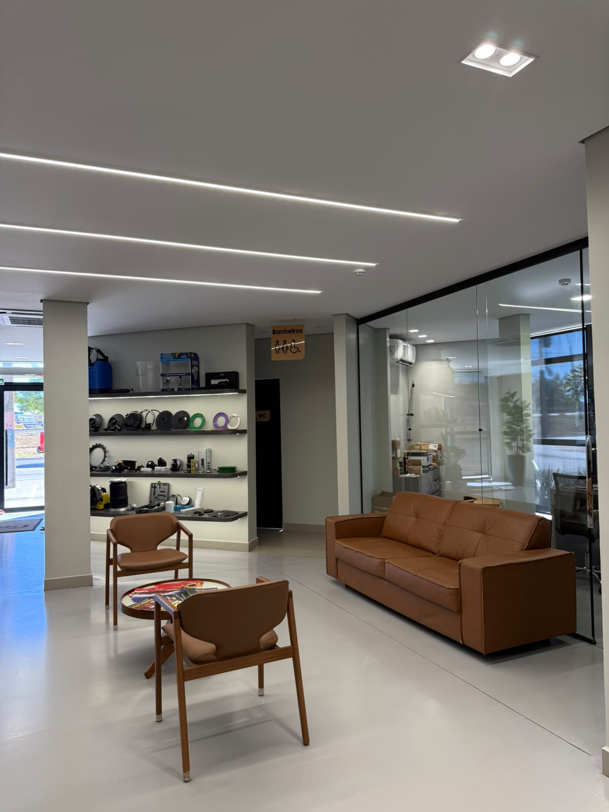 Lounge de espera com sofá de couro caramelo e prateleira de peças ao fundo