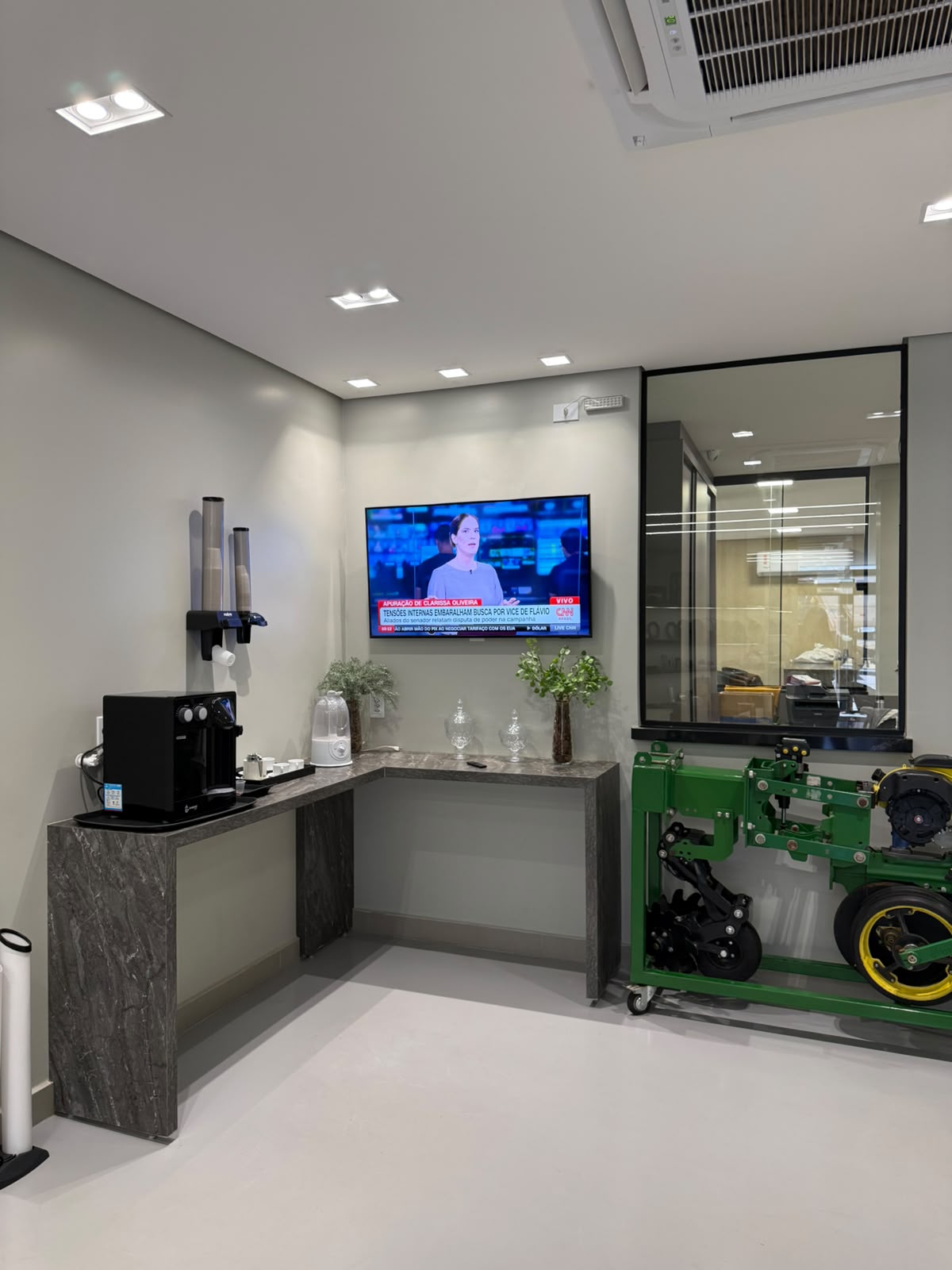 Sala com televisão, dispenser de copos e módulo de plantadeira John Deere